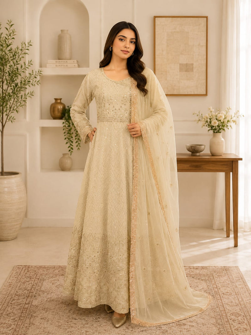 Ivory off-white Anarkali gown with all-over gold thread and sequin embroidery, paired with matching net dupatta, worn by model in a modern interior setting
